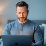 A man using a laptop at home in private, representing online erectile dysfunction care through a Canadian digital clinic.